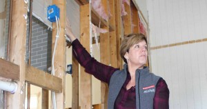 Sarah Kirby pointing to drywall behind exposed wooden studs in a flooded home.